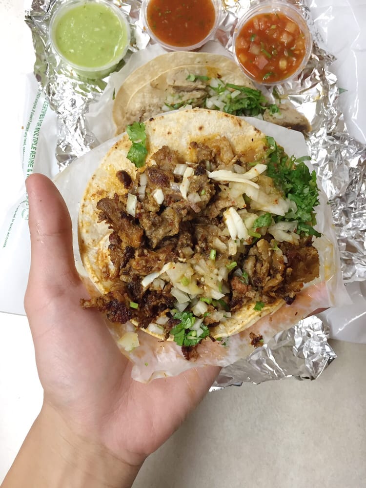 Al pastor tacos with onions and cilantro served with green and red salsa cups