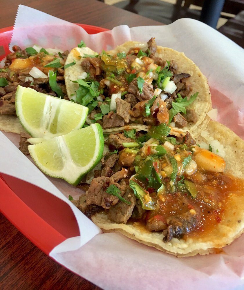Carne asada tacos on corn tortillas with salsa, cilantro, onions, and lime wedges