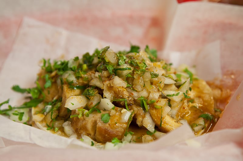 Carnitas topped with fresh cilantro and diced onions served in a paper-lined basket