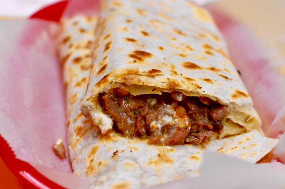 Super burrito cut in half showing beans, meat, cheese, and sour cream in a toasted flour tortilla